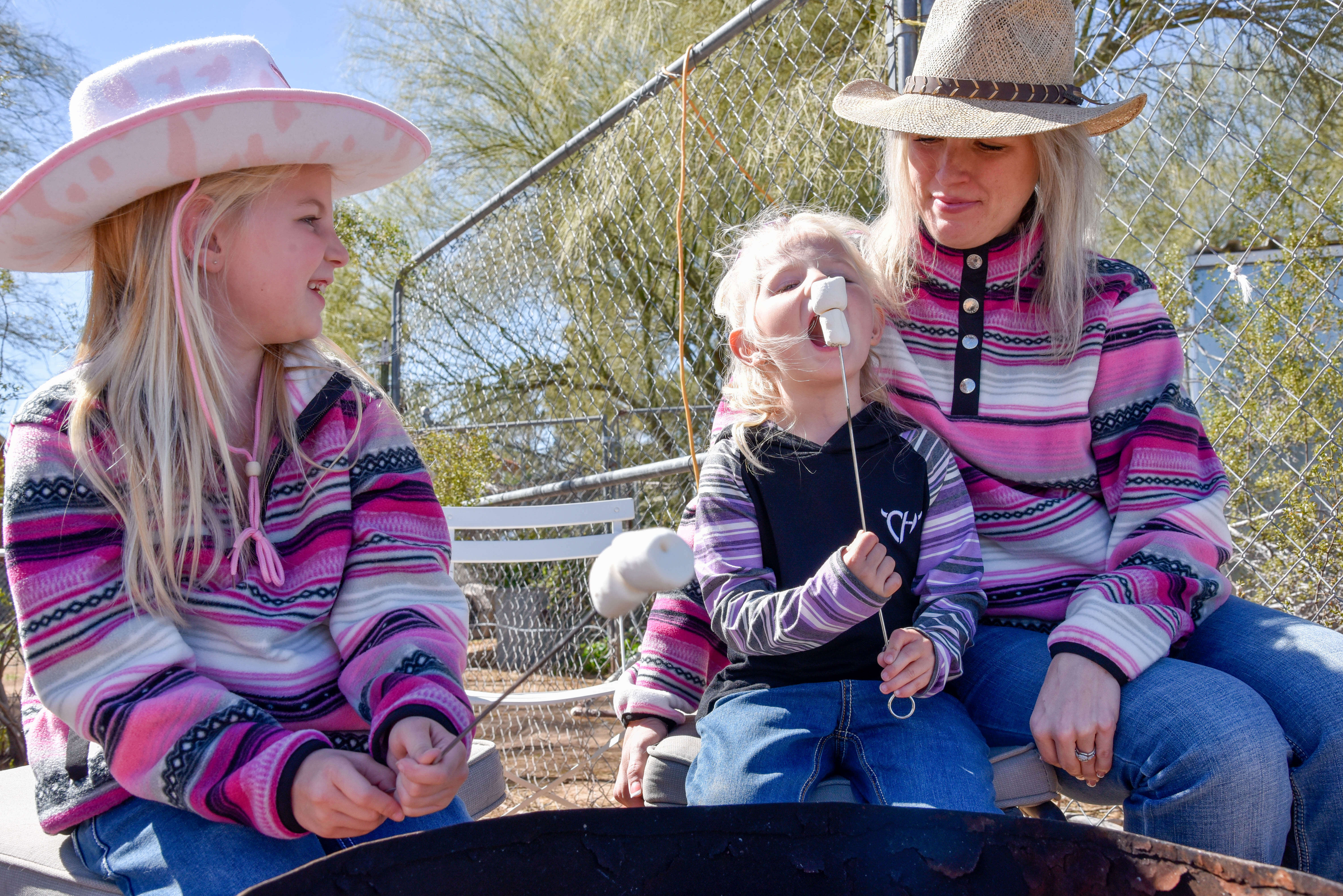 Mother cowgirl and her two daughters roasting marshmallows in their new Fall 2023 western wear clothes from Cowboy & Cowgirl Hardware