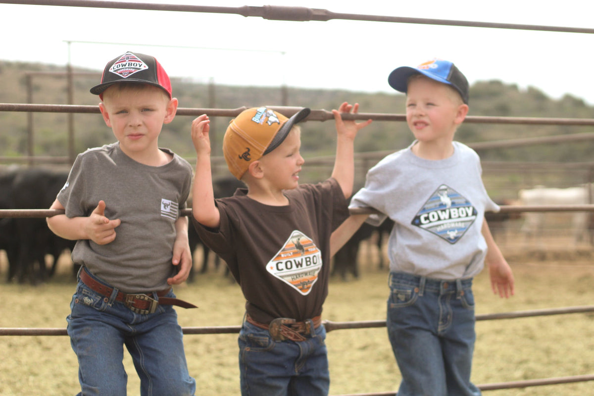 Young cowboys hanging on the fence in the corral wearing Cowboy Hardware boy t-shirts