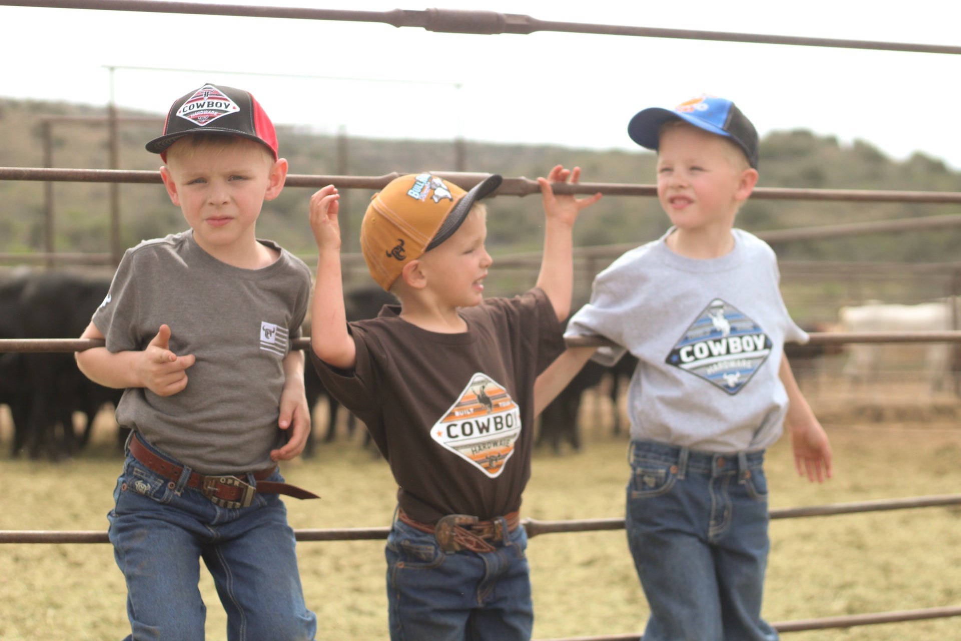 Young cowboys hanging on the fence in the corral wearing Cowboy Hardware boy t-shirts