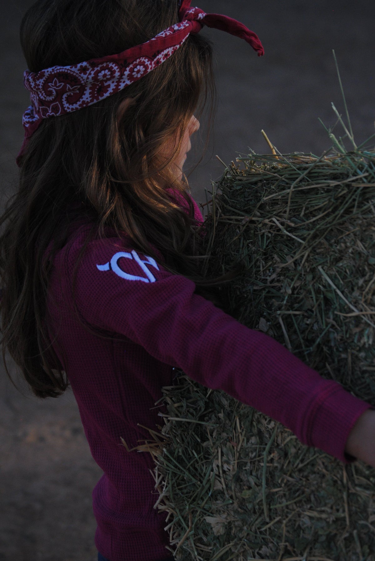 Young cowgirl moving hay while wearing a CH girls western top.