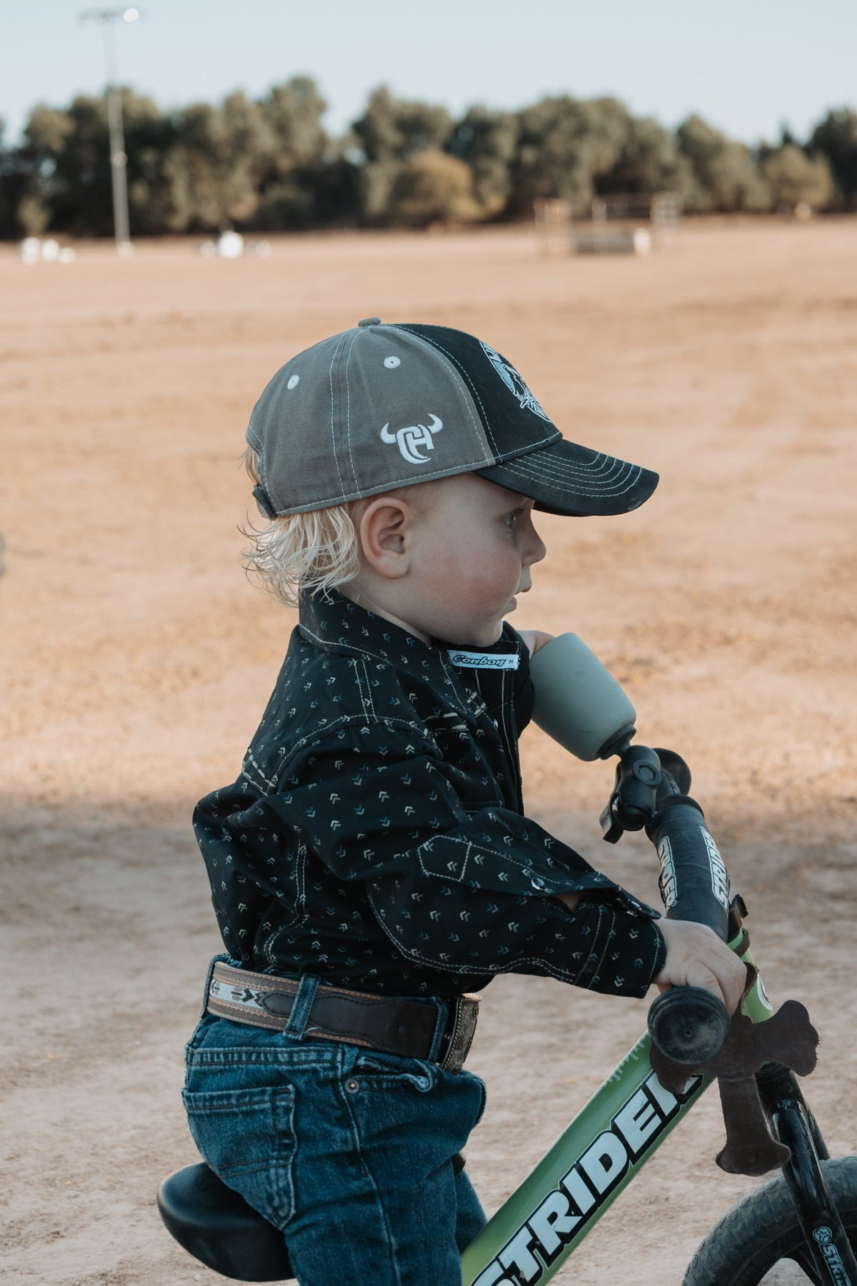 Young cowboy riding his bike on the farm while wearing a CH infant and toddler boys cap.