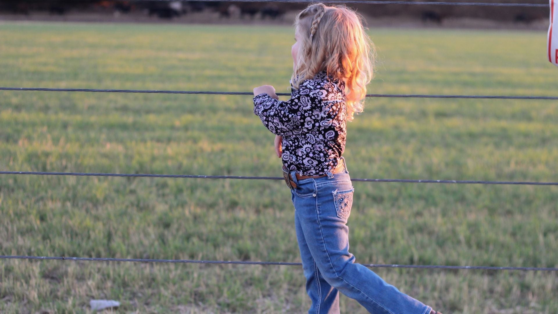 Little cowgirl standing on fence wearing an infant and toddler western shirt from Cowgirl Hardware