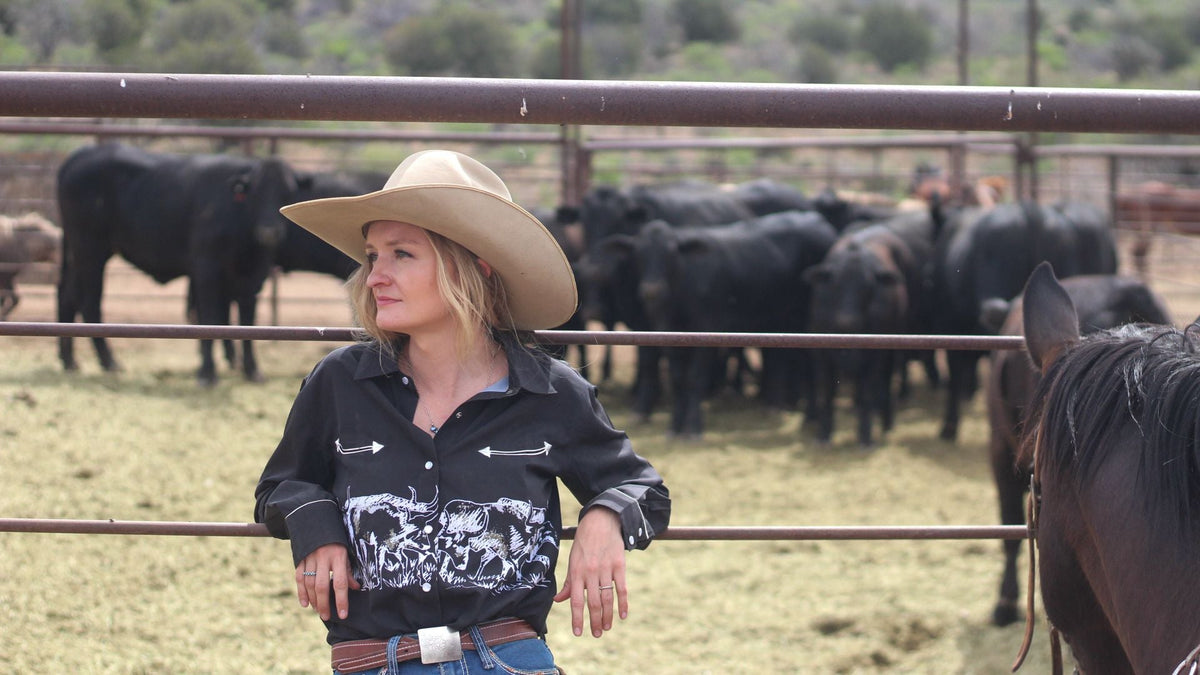 Cowgirl leaning on corral railing wearing a western shirt from Cowgirl Hardware