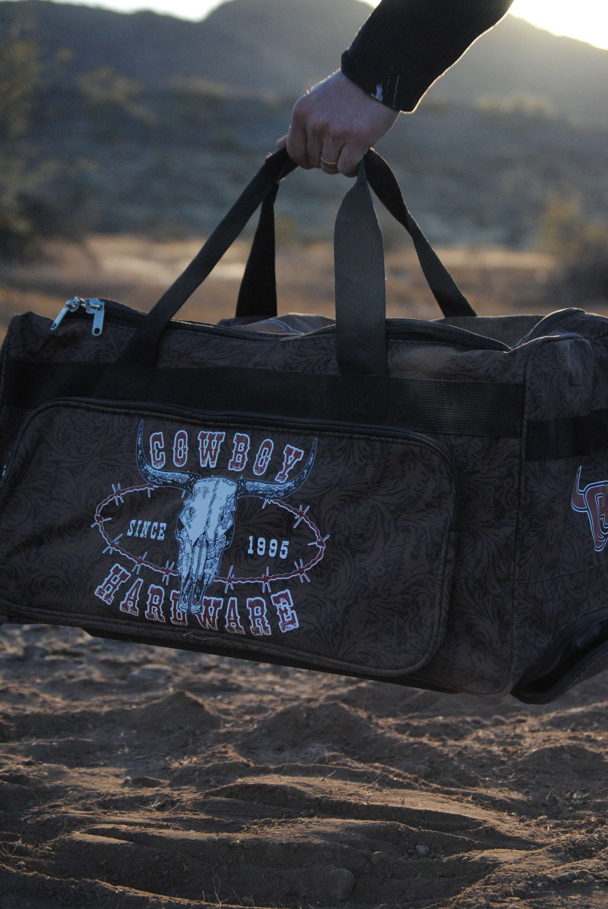CH Outlaw Since 95' 3 Wheel Gear Bag being held by Cowboy from Cowboy Hardware