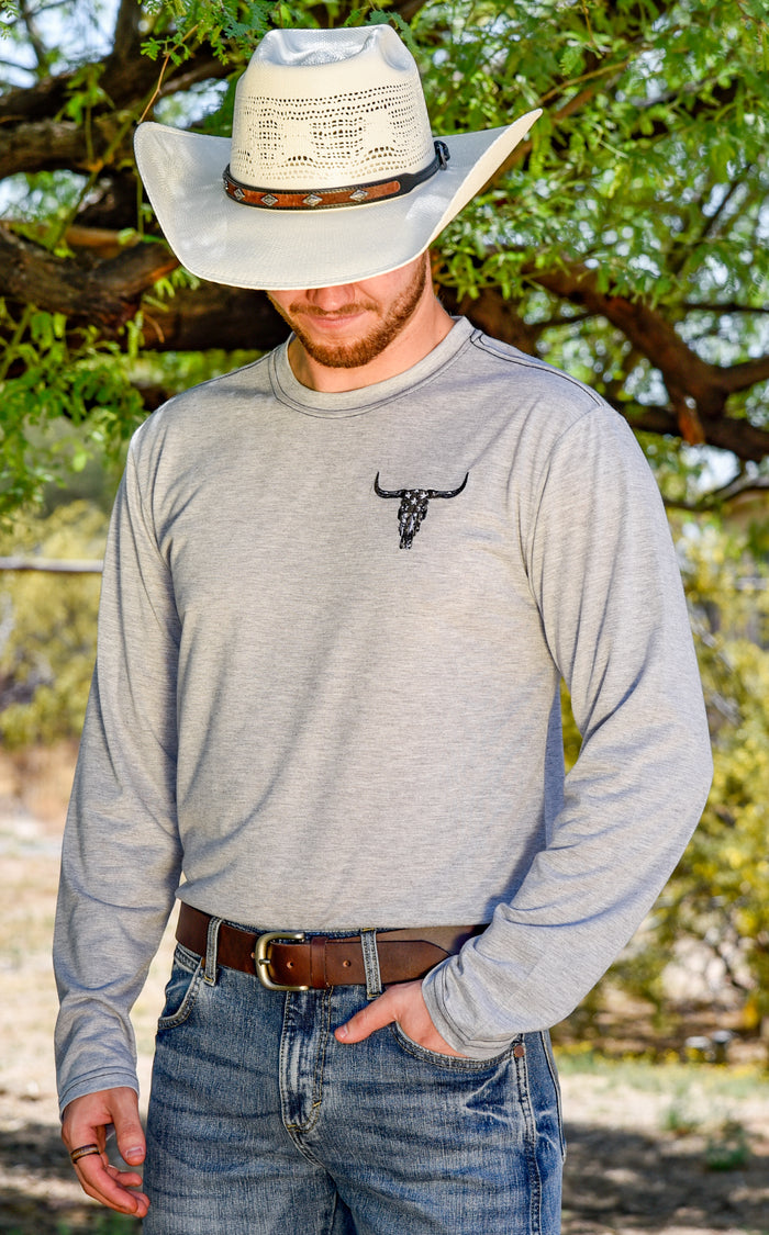 Cowboy wearing gray flag skull long sleeve in front of ranch