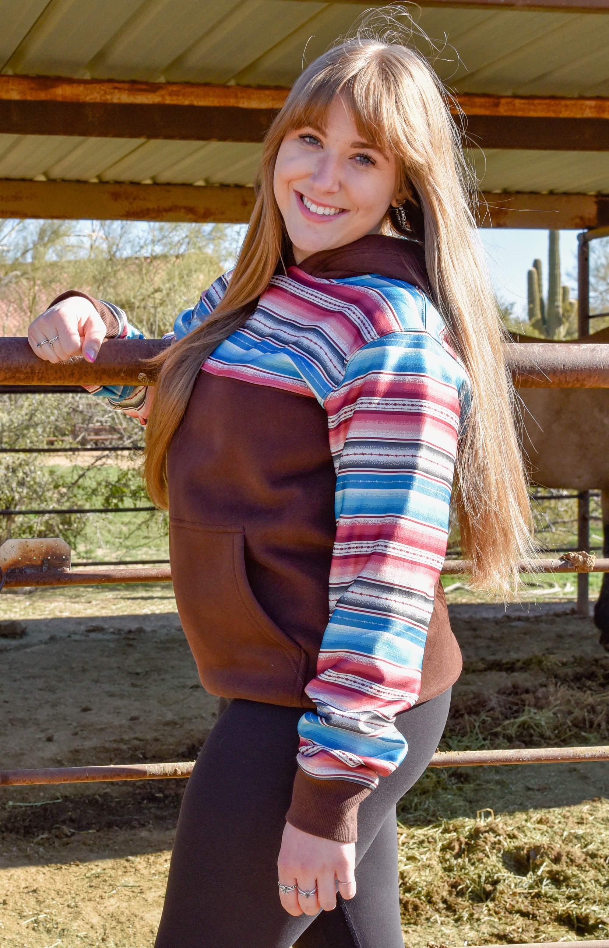 cowgirl standing in front of the corral wearing CH Dark Chocolate "Serape Yoke" Fleece Hoodie from Cowboy Hardware
