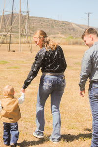 Family of three walking together in a field with mountains in the background