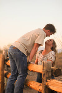 Cowboy kissing his cowgirl, wearing a Men's Cowboy Hardware Desert Sand "Buck Shack" Short Sleeve T-Shirt.