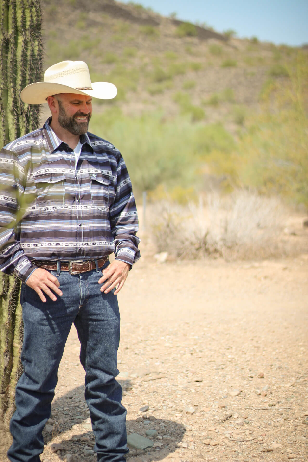 A cowboy is relaxing in the desert wearing a CH navy striped Aztec long sleeve print Western shirt.