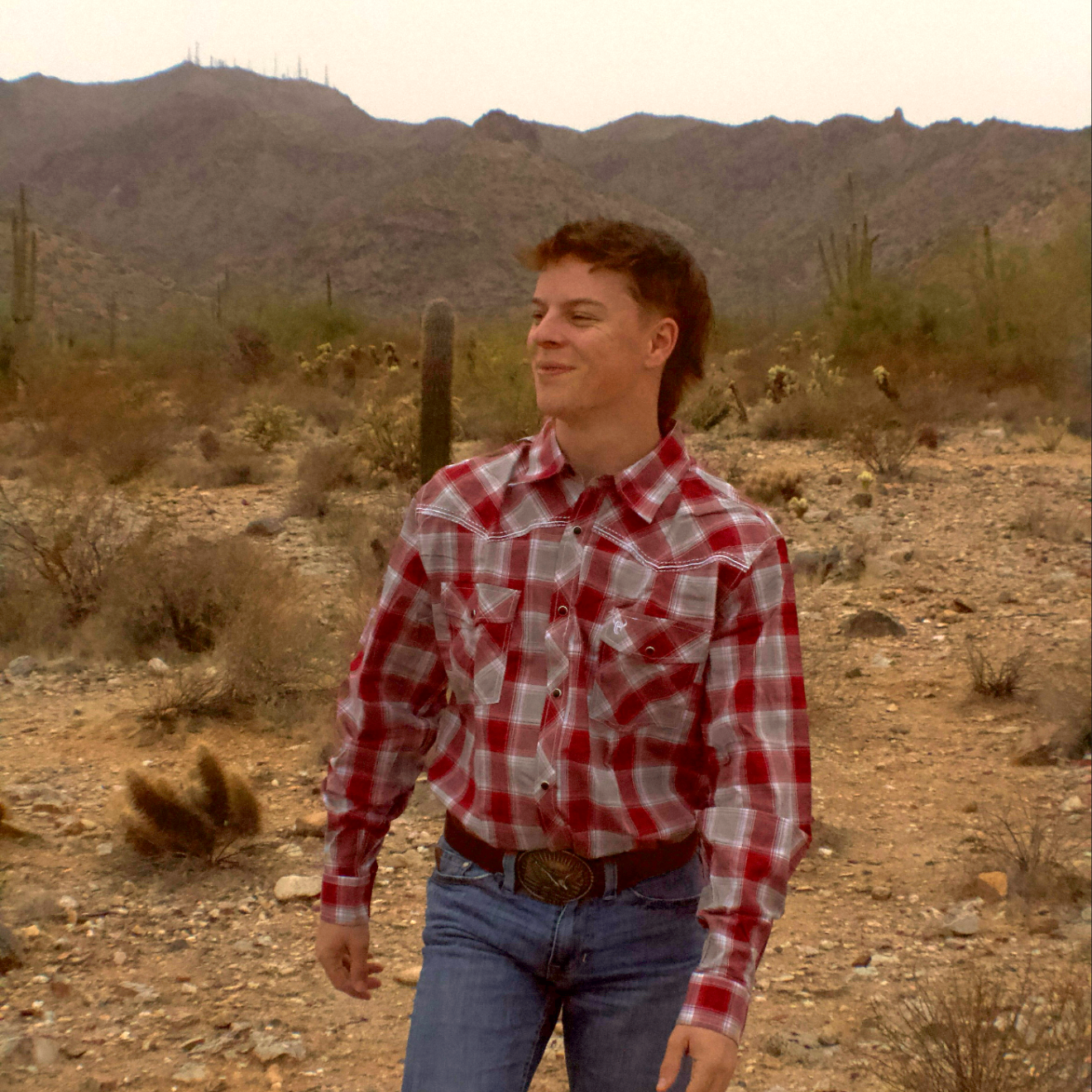 Cowboy smiling and walking through the Arizona desert wearing Cowboy Hardware's Hombre Chili Long Sleeve Plaid Western Shirt