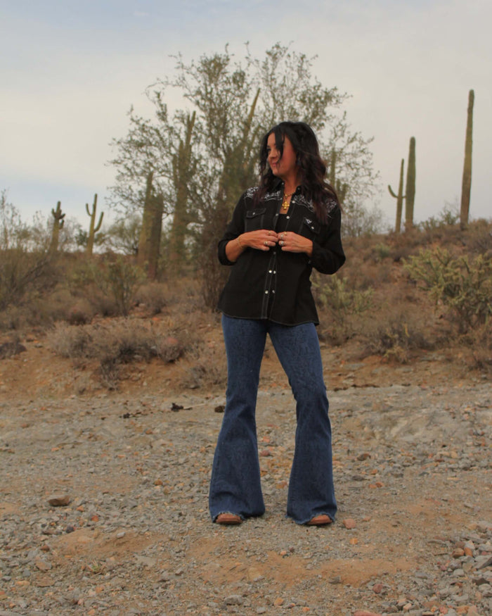Cowgirl posing wearing women's CH tooled leather medium washed bell bottoms jeans from cowgirl hardware with a cute top in the Arizona desert