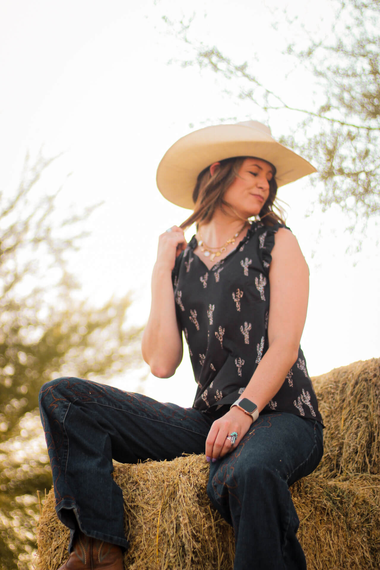 Cowgirl relaxing on some hay while wearing Women's Cowgirl Hardware Leopard Saguaro Black Ruffle V-neck Tank.