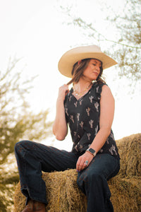 Cowgirl relaxing on some hay while wearing Women's Cowgirl Hardware Leopard Saguaro Black Ruffle V-neck Tank.