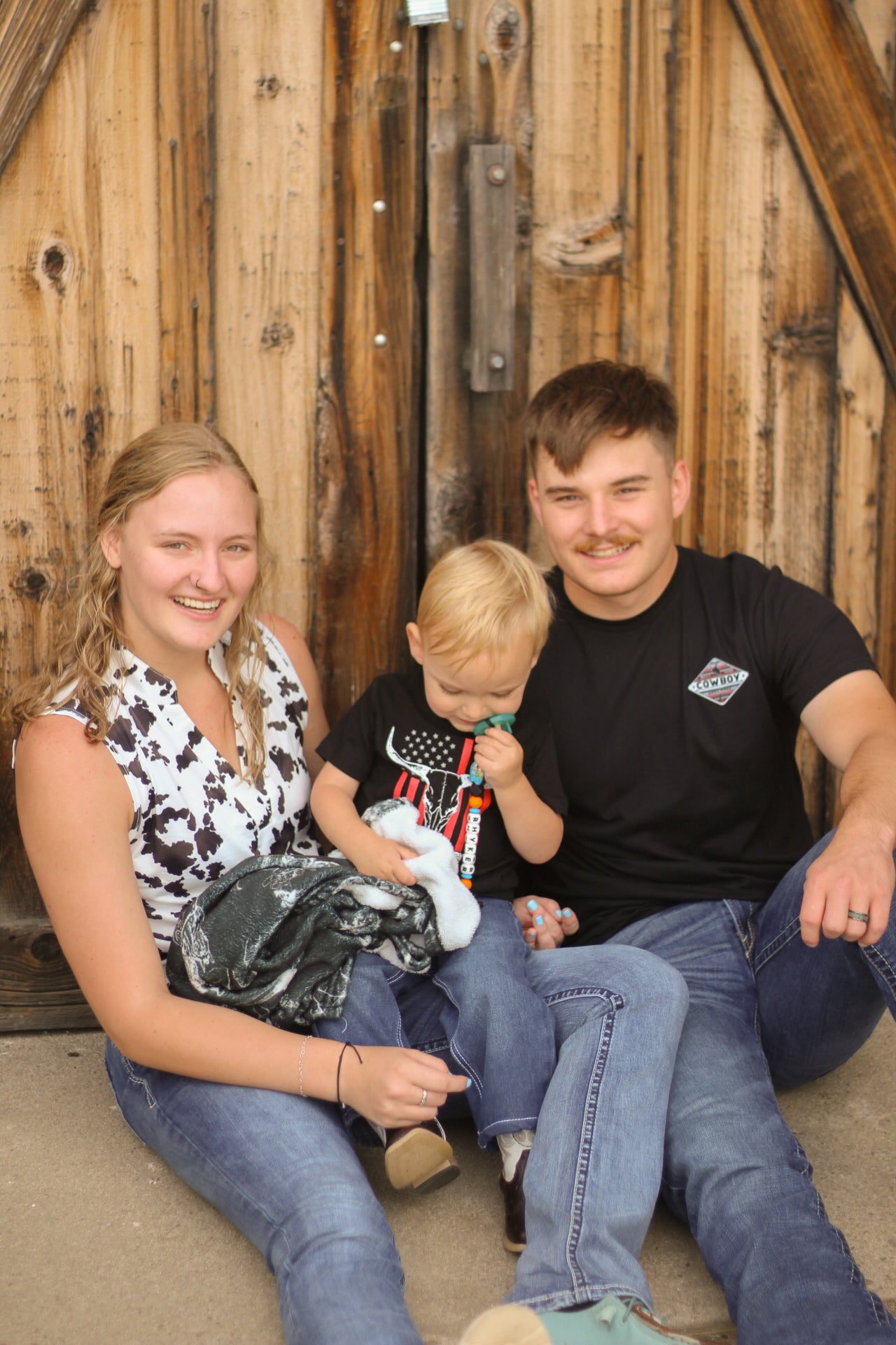 Family of three sitting together in front of a wooden wall.