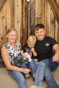 Family of three sitting together in front of a wooden wall.