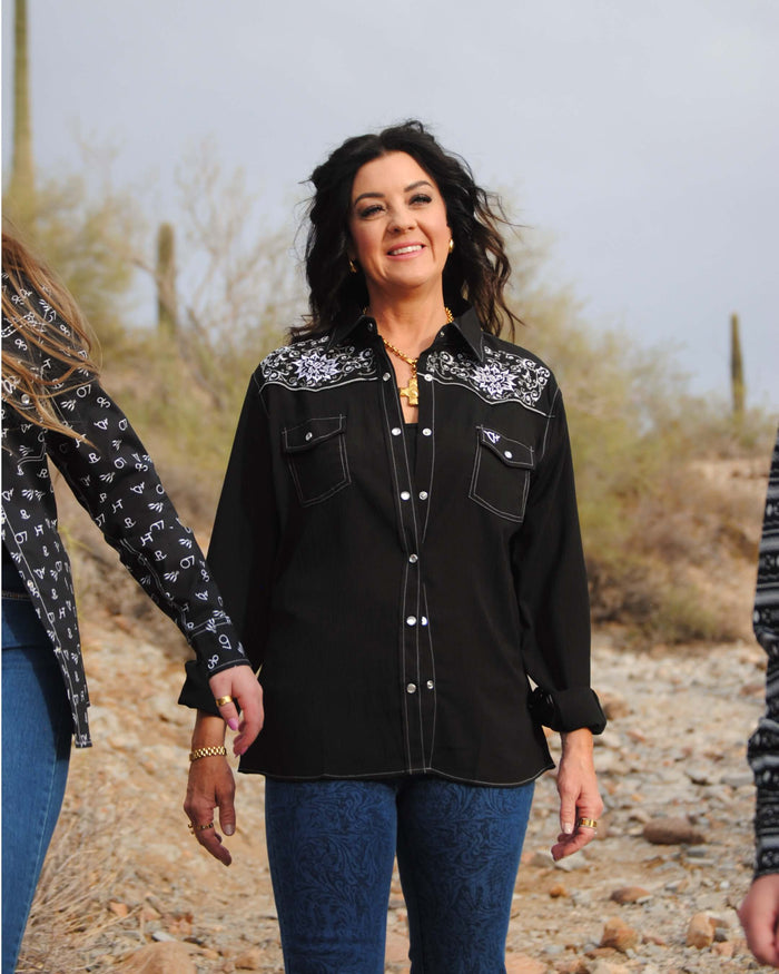 Lady walking thorugh desert with others smiling at camera wearing Cowgirl Hardwares black vintage embroidered long sleeve solid western shirt