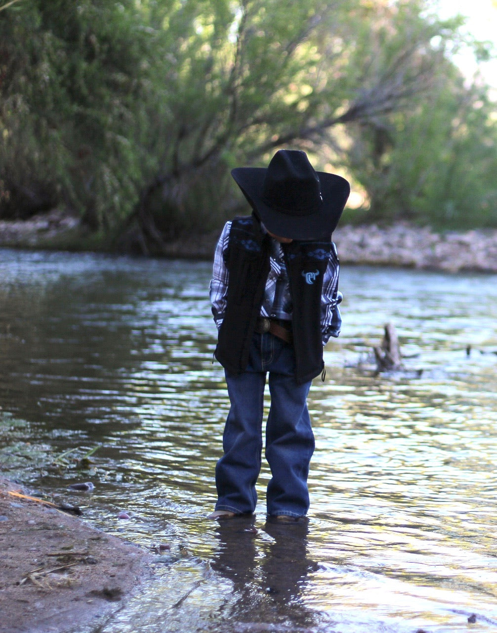 Little Cowboy standing in creek wearing Cowboy Hardware's tonal aztec accent black poly shell vest