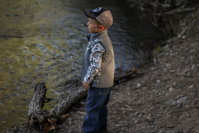 Little cowboy staring at creek wearing boy's Cowboy Hardware tonal aztec accent grey poly shell vest