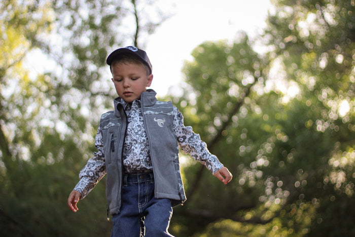 Little cowboy wearing boy's Cowboy Hardware tonal aztec accent grey poly shell vest walking through the woods