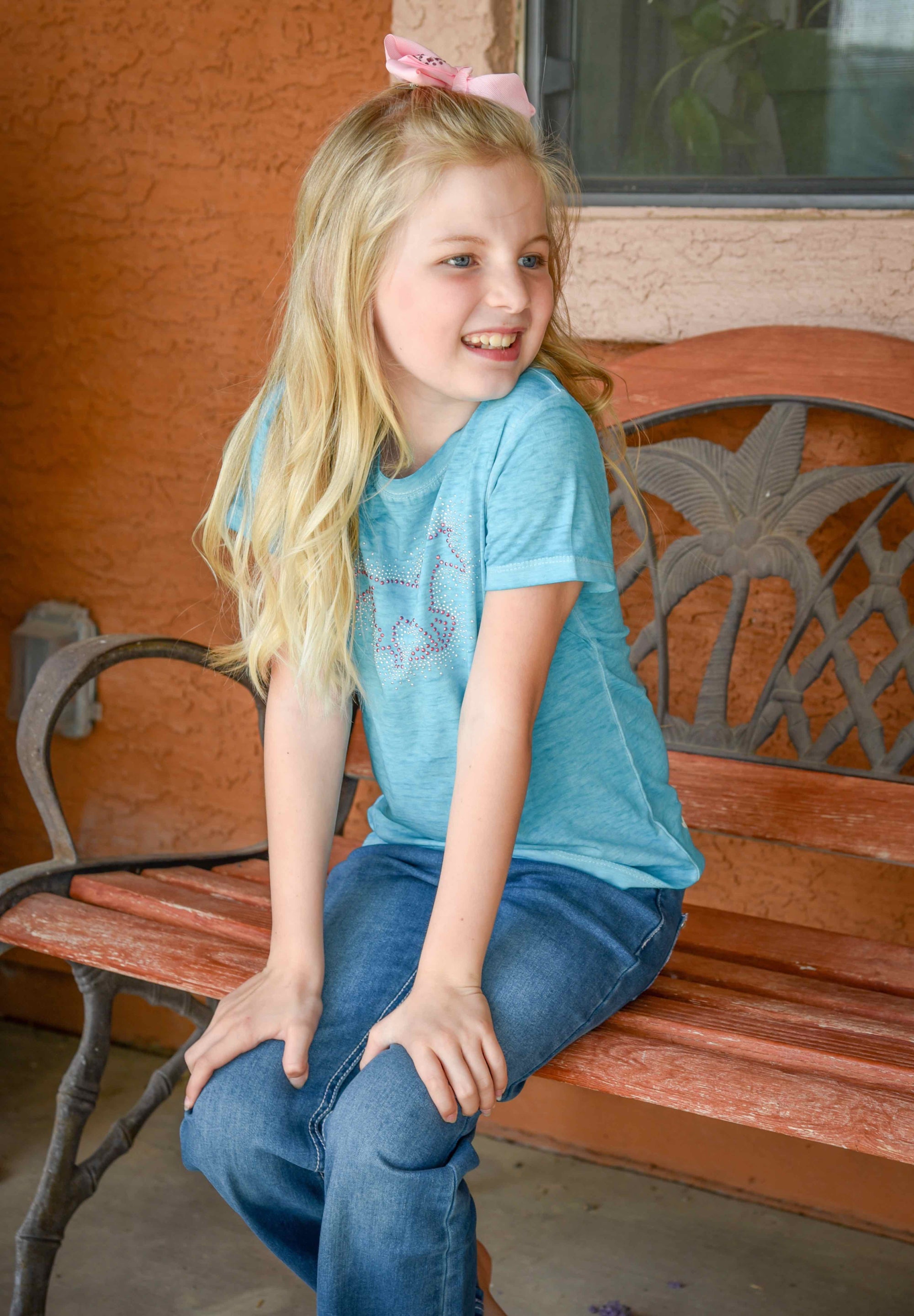 Little cowgirl sitting on front porch bench wearing Cowgirl Hardware's infant and toddler girls turquoise acid wash crew neck shorts sleeve top