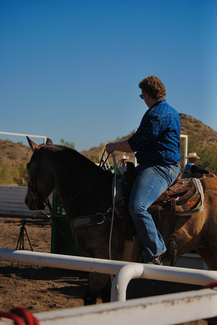 Side angle of cowboy riding horse in Cowboy Hardware's navy skull burst long sleeve western shirt