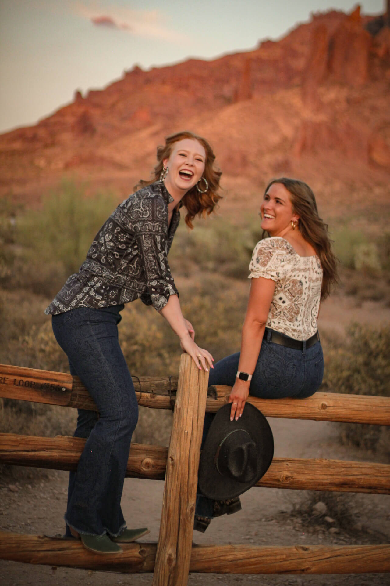 Two cowgirls laughing while wearing a women’s Cowgirl Hardware Black & Grey Patchwork Bandana Hi-Lo Top.