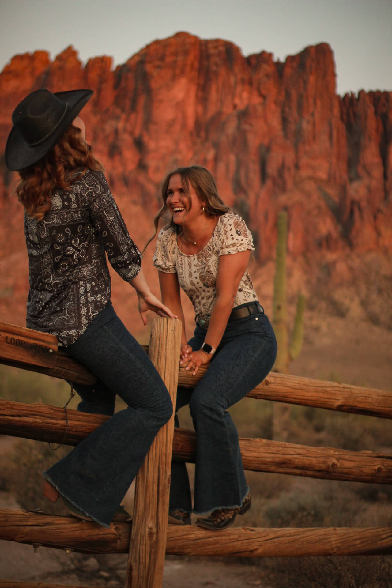 Two cowgirls laughing outside while wearing women’s Patchwork Bandana Short Sleeve Blouse from Cowgirl Hardware.