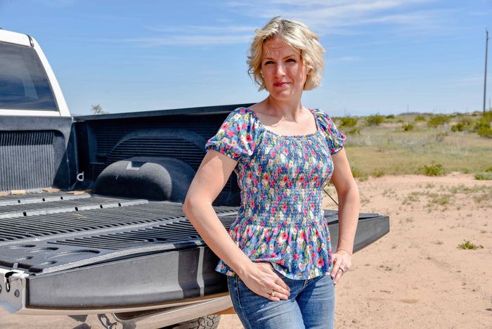 Woman leaning on truck bed in the desert wearing Cowgirl Hardware's navy pink and white floral monet short sleeve smock top