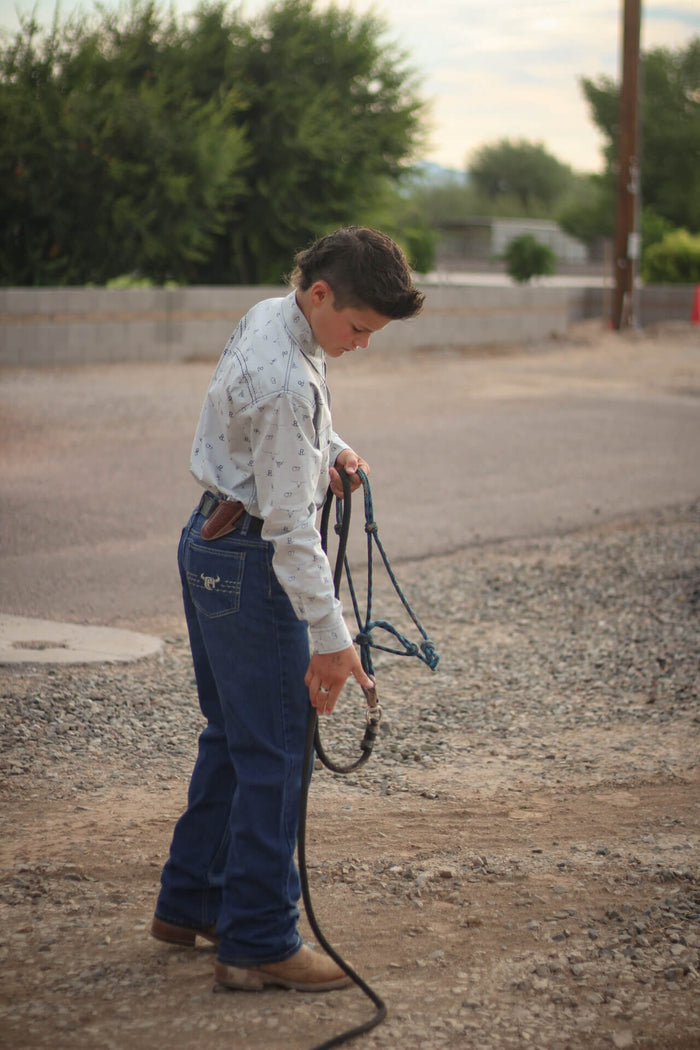 Young cowboy about to put a bridle on a horse.
