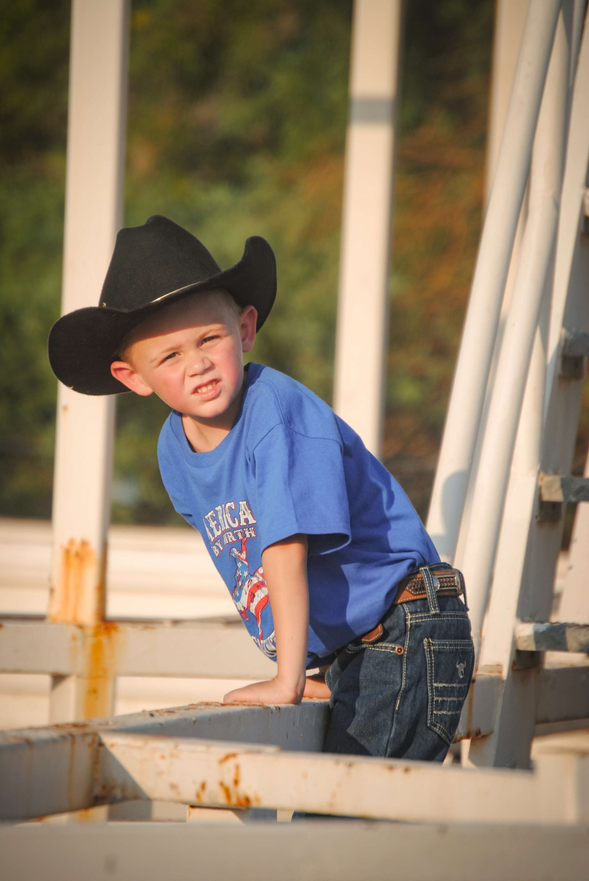 Young cowboy checking on his farm animals wearing Youth Boys Cowboy Hardware Royal Blue American By Birth Short Sleeve Tee.
