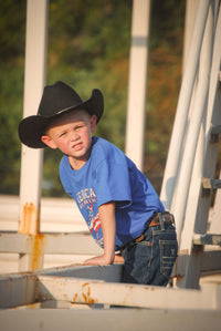 Young cowboy checking on his farm animals wearing Youth Boys Cowboy Hardware Royal Blue American By Birth Short Sleeve Tee.