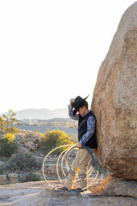 Young cowboy leaning against a boulder with rope after a hard day on the ranch.