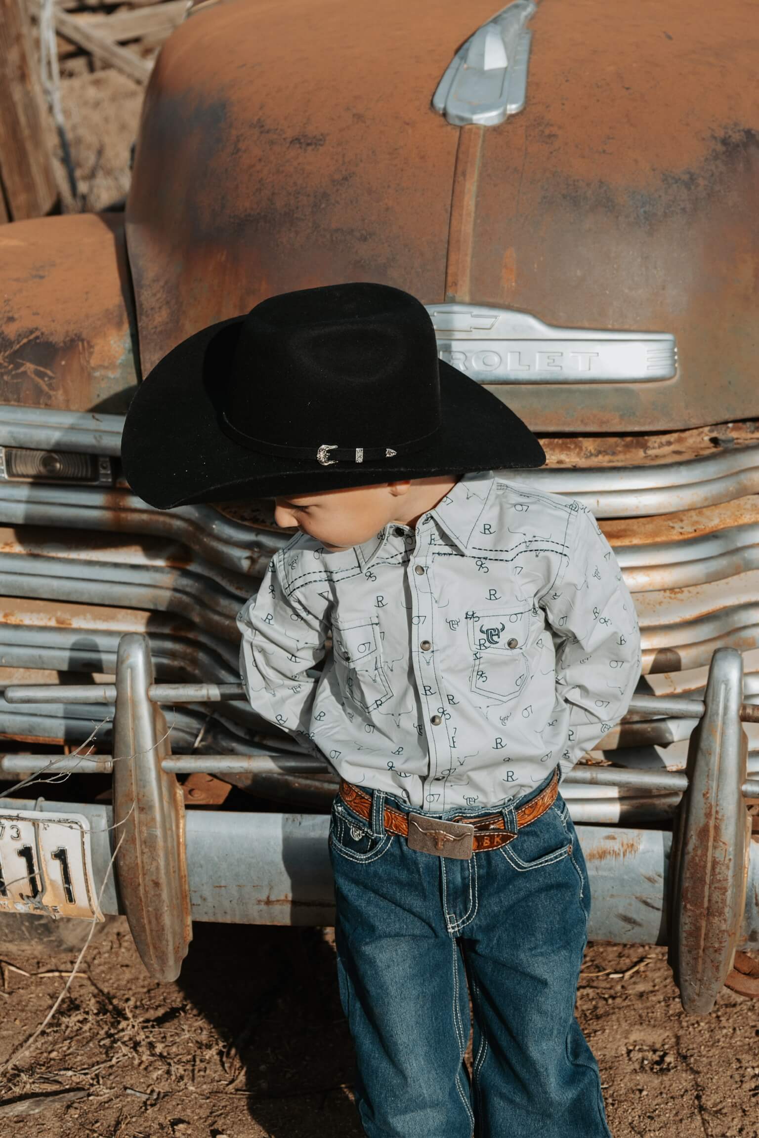 Young cowboy leaning against an old truck.