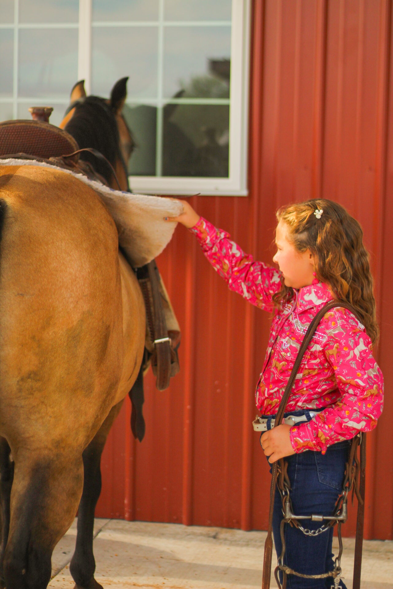 Young cowgirl saddling up her horse.